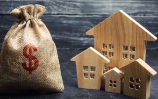 Image of a burlap sack with a red dollar sign and wooden house cutouts on a dark background.