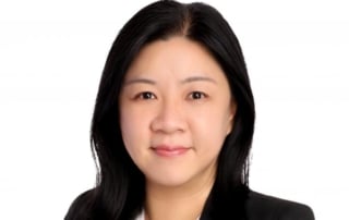 Businesswoman with medium-length black hair wearing a white blouse and dark blazer, facing the camera