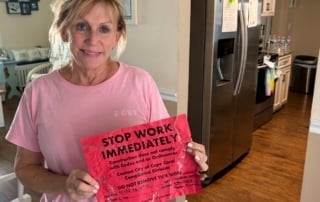 A woman holding a "stop work immediately" notice in a kitchen.