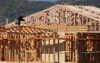 Construction site featuring framework of a single-family house with a worker wearing safety gear