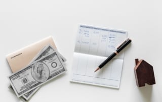 Image of a cashbook, checkbook, and a house-shaped cutout symbolizing financial planning and real estate investment