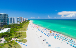 A vibrant beach scene in florida with ocean, sand, umbrellas, and cityscape