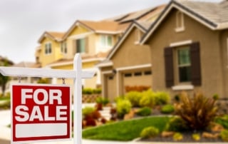 Photo of a "for sale" sign with suburban houses in the background