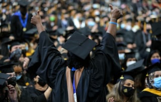 A graduate in cap and gown celebrates at a graduation ceremony with thumbs up, symbolizing student debt relief success.