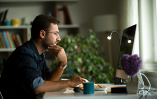 Man sitting at a desk in a home office, focused on his computer screen.