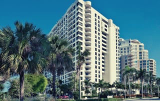 A modern multi-story residential building under a blue sky with palm trees.