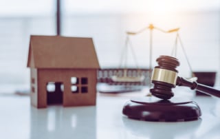 Close-up of a gavel with a model house and justice scales in the background