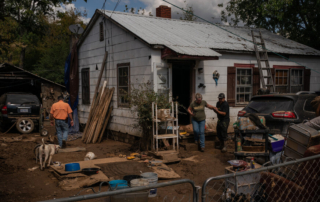 The front yard of a weathered house with repair efforts underway, capturing a story of survival and rebuilding.