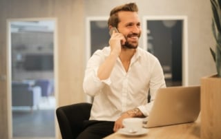 Man in tattooed arms smiling and talking on smartphone at office