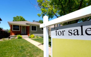 Image of a single-story suburban house with a "for sale" sign in the foreground, clear blue sky above, highlighting the real estate market.