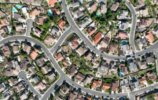 Aerial view of a suburban neighborhood with diverse single-family homes, green lawns, and winding streets.