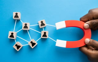 Hands holding a red horseshoe magnet towards wooden blocks representing connections