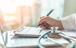 Close-up of hand writing on a clipboard in a telehealth setting