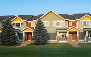 A row of townhouses with gabled roofs and evergreen trees under a clear blue sky.