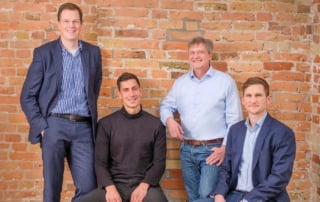 Four men in business attire posed against a brick wall