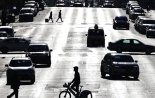 Image of a busy city street scene with cars, cyclist, and pedestrians