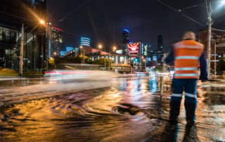 A worker in a high-visibility vest managing floodwater on a city street at night