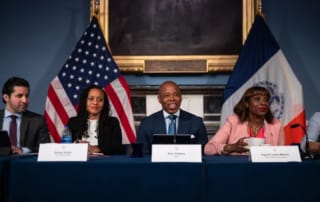 Officials seated at a table with american and nyc flags