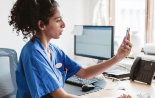 Nurse conducting a telehealth consultation via smartphone in an office setting.