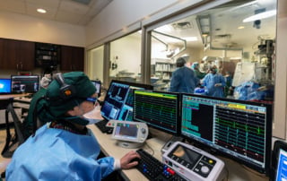 Image of a medical professional in a cardiac lab analyzing heart rhythms on computer monitors