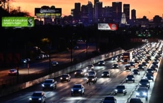 Image of a busy highway during twilight with cars and a truck against the los angeles skyline.