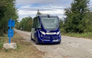 A navya-designed driverless shuttle travels along a rural road, surrounded by greenery