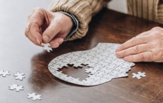 Elderly person working on a brain-shaped jigsaw puzzle on a wooden table