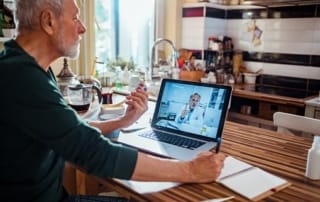 Older man engaging in telehealth consultation from kitchen
