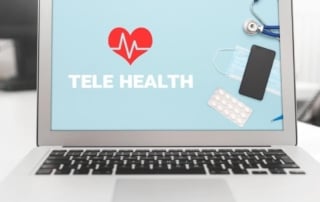 Image of a laptop screen displaying 'tele health' with healthcare items nearby