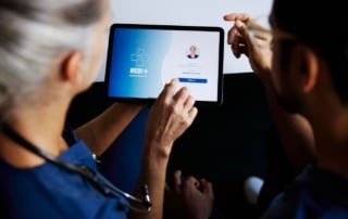 Image of two medical professionals in a clinical setting using a tablet for patient records