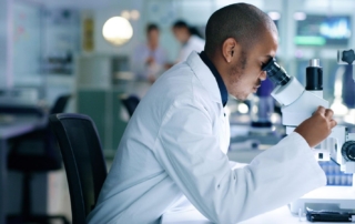 Person in lab coat using a microscope in a research lab