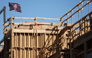 Construction site under a clear blue sky with a wooden framework for multifamily housing, featuring an american flag.