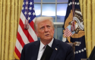 Man in suit at desk with american and eagle-emblem flags