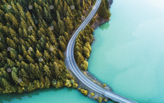 An aerial view of a scenic landscape with a winding road through a forest and body of water.