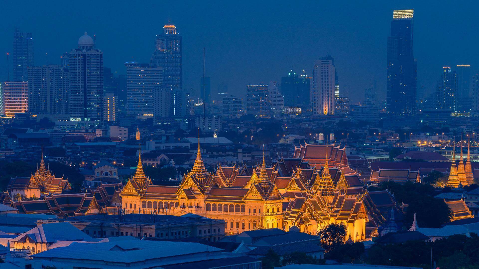 A night view of Bangkok, featuring the illuminated Grand Palace architecture against a modern skyline.