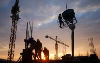 Image of a construction site at sunset with workers and cranes