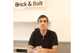 A man at his office desk with "brick & bolt home construction" sign in background