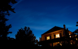 A night-time view of a two-story house illuminated by warm light against a starry sky backdrop.