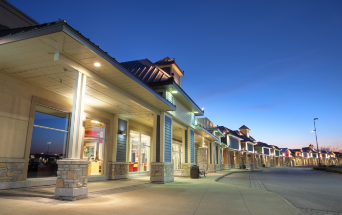 Strip mall with metal roofs and illuminated storefronts at dusk