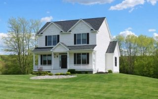 A modern two-story white house with dark shutters set in a lush, green landscape in new hampshire.