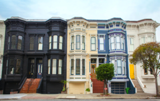 A row of colorful victorian-style townhouses with black, beige, blue, and white facades