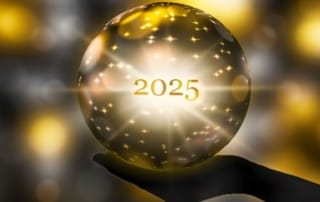 A silhouetted hand holding a glowing crystal ball with the year 2025 illuminated inside, representing future predictions.