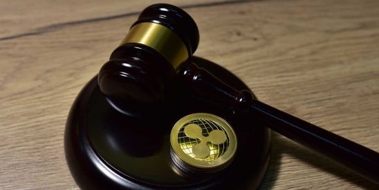 Image of a judge's gavel alongside a digital asset coin on a wooden surface