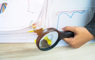 Hand holding a magnifying glass over financial documents