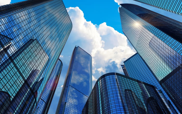 Upward view of modern skyscrapers with glass facades and a vibrant blue sky.