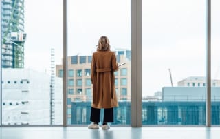 Person standing in front of large windows overlooking a developing cityscape