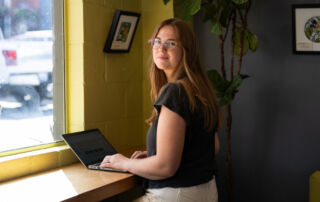 A person with long hair using a laptop in a well-lit cafe