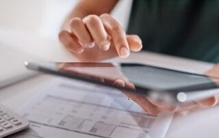 Close-up view of hands interacting with a tablet device next to a financial document and calculator, representing modern digital financial management.