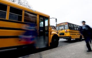 Image of yellow school buses at a school pickup area with nearby figures, suggesting activity and motion.