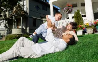 A family enjoys a playful moment on a well-kept lawn in front of a charming house.